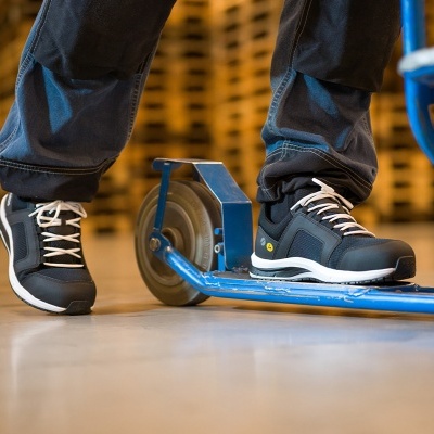 Ténis de segurança pretos com detalhes brancos e equipamento azul no chão da fábrica