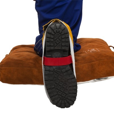 Sapatilha de escalada preta com faixa vermelha e bordas amarelas sobre almofada castanha