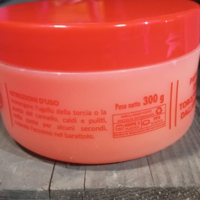 Frasco plástico com tampa vermelha e texto em italiano