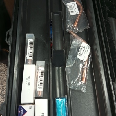 Cabos e conectores de cobre embalados em plástico e papelão sobre suporte preto.