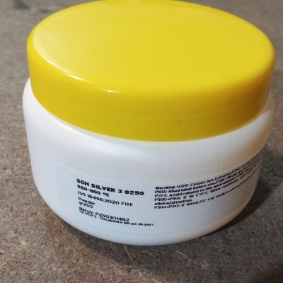 Frasco plástico branco com tampa amarela e texto preto sobre superfície cinzenta