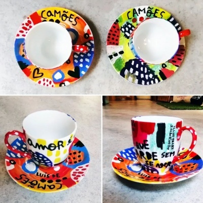 Duas chávenas de café coloridas com pires, decoradas com padrões geométricos e texto