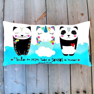 Almofada branca com desenhos de gato, unicórnio e panda e texto em português.