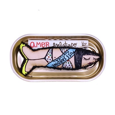 Boneca de tecido com maiô colorido em forma de peixe dentro de lata dourada com etiquetas