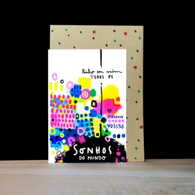 Cartão colorido com texto em português apoiado em suporte com pontos coloridos sobre mesa de madeira