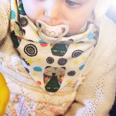 Bebé com babete colorido de coruja e chupeta branca