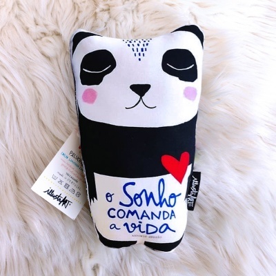 Almofada em formato de panda com frase inspiradora vermelha e azul sobre fundo branco e preto
