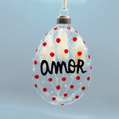 Ornamento oval transparente com bolinhas vermelhas e brancas e a palavra 'amor'