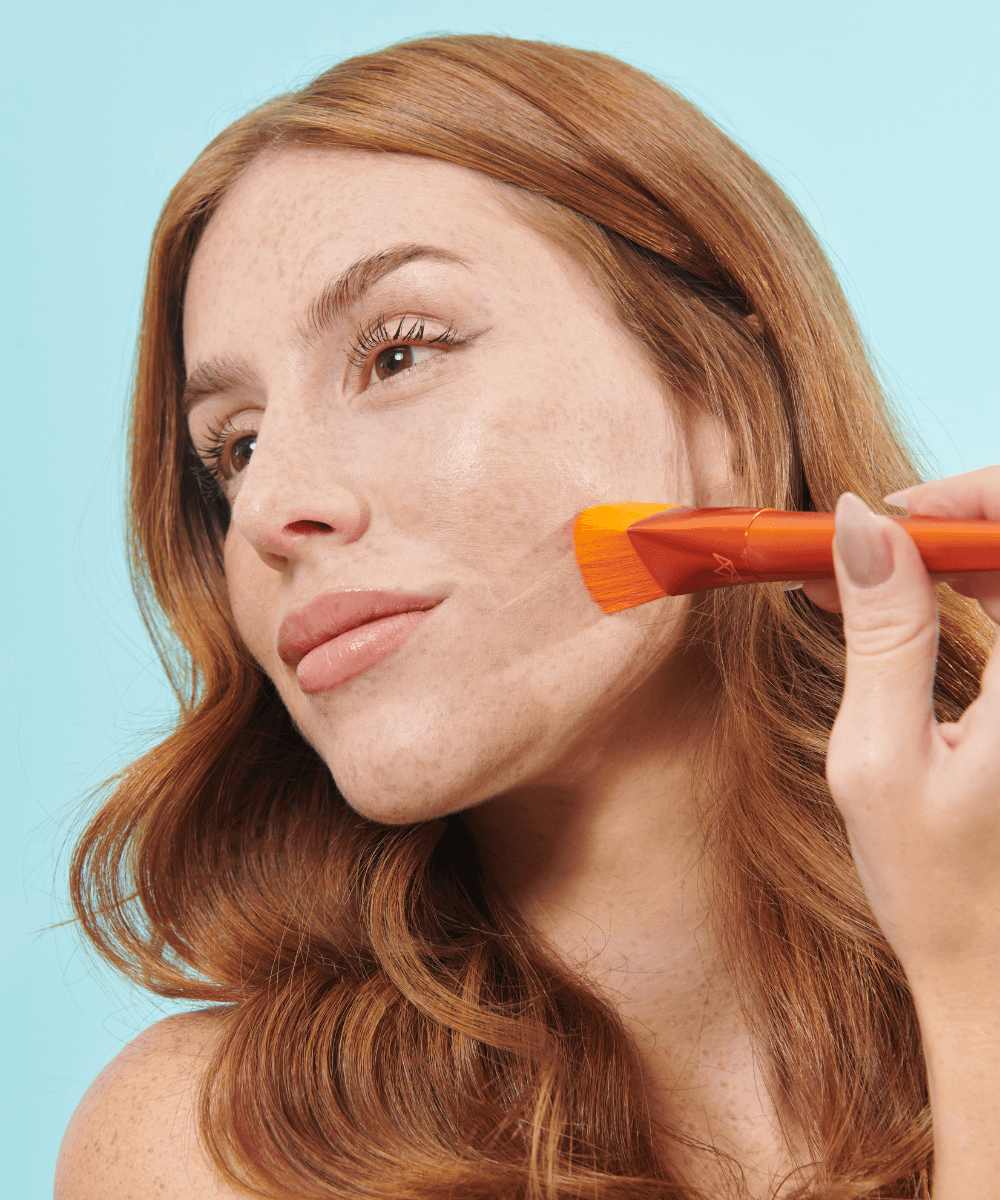Pincel Triangular Para Base 105 - Mari Maria Makeup Mulher ruiva aplicando maquilhagem com pincel laranja