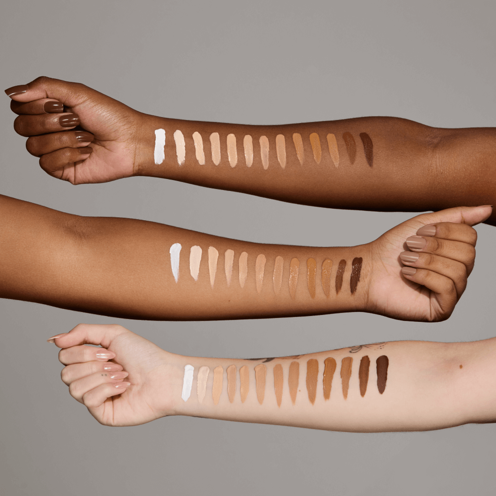 Corretivo Camuflagem Alta Cobertura Angel Wings - Catharine Hill Três braços com amostras de bases de maquilhagem em várias tonalidades desde branco a castanho escuro