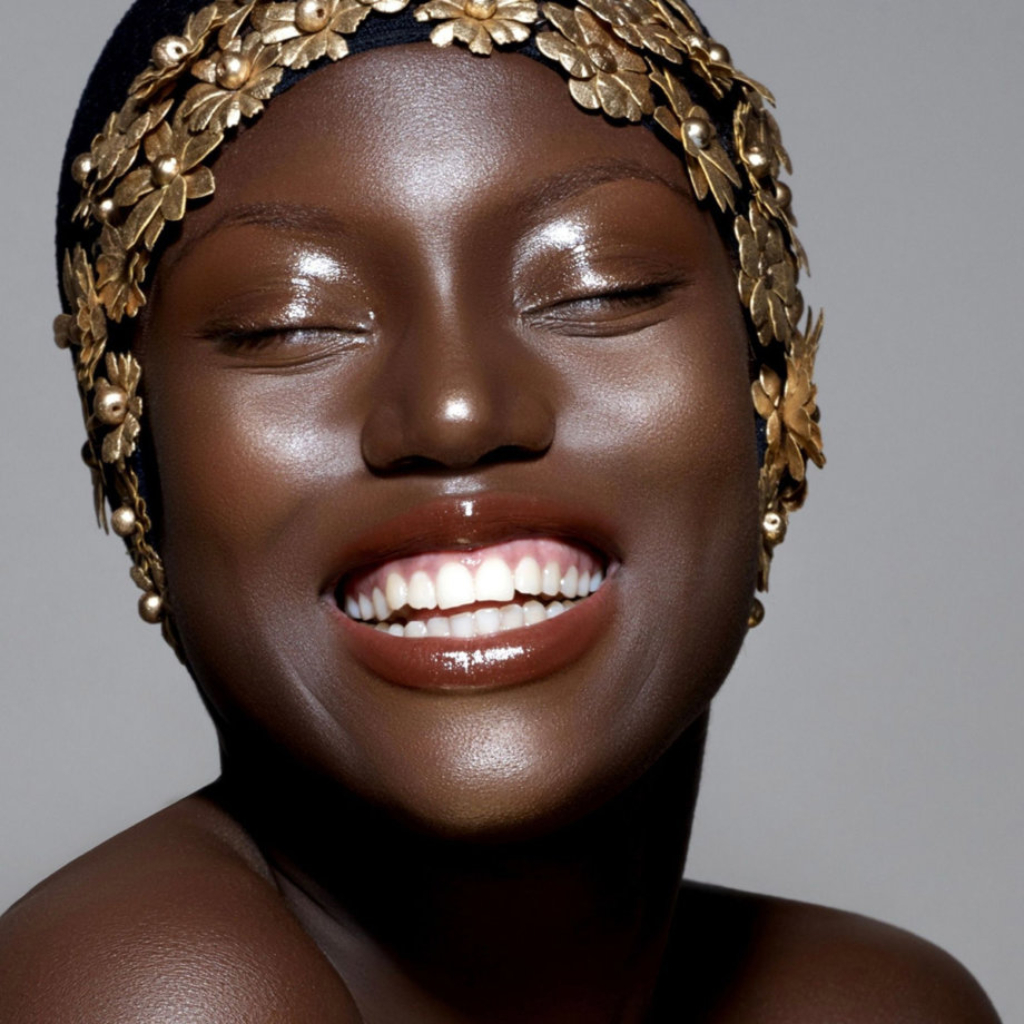 Dew Wet Balm Danessa Myricks Beauty Rosto feminino com faixa preta com flores douradas e sorriso grande