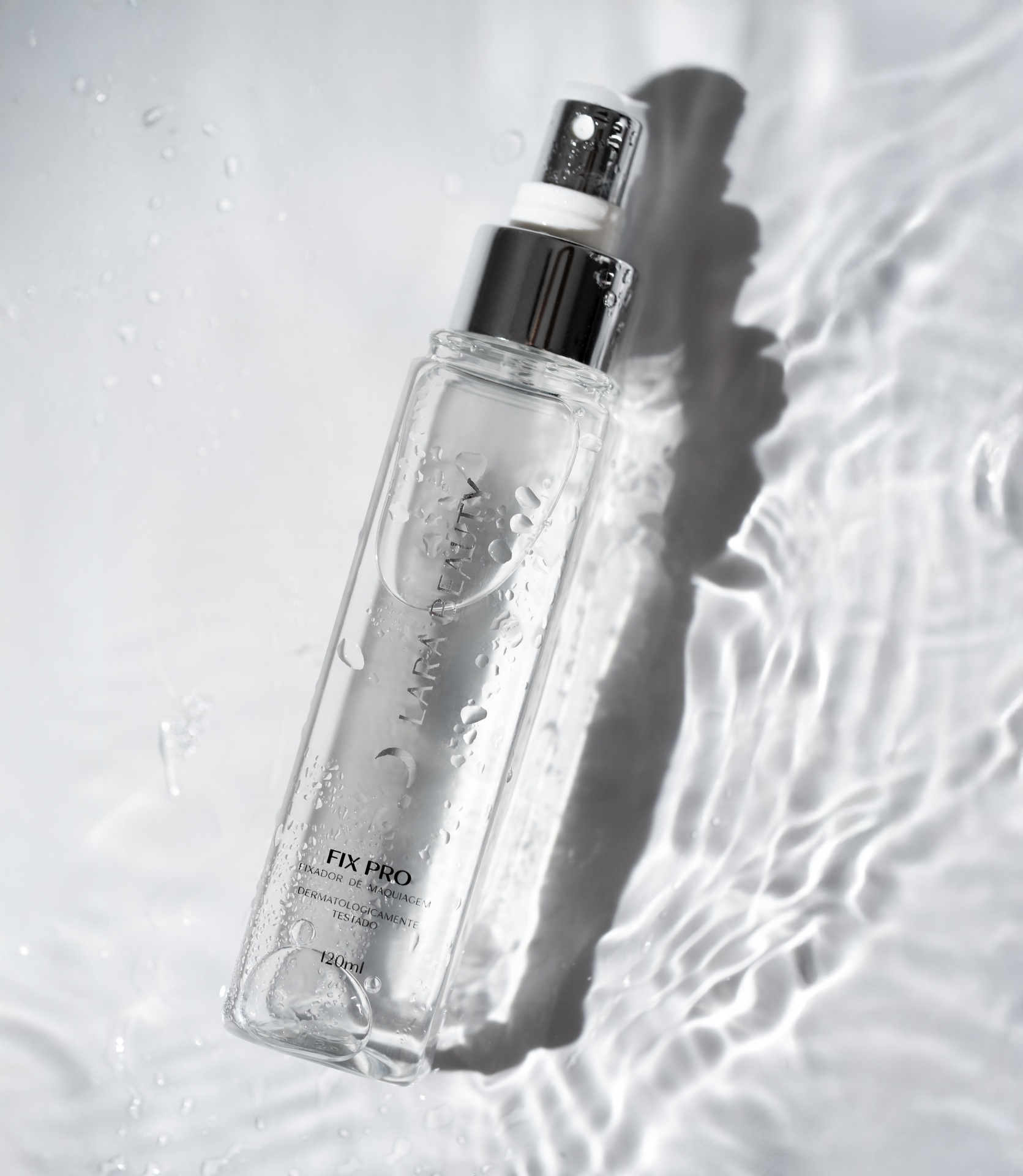 Fix Pro Fixador de Maquilhagem 120ML Lara Beauty Frasco de spray transparente com tampa prateada e gotas de água em fundo branco com reflexos.