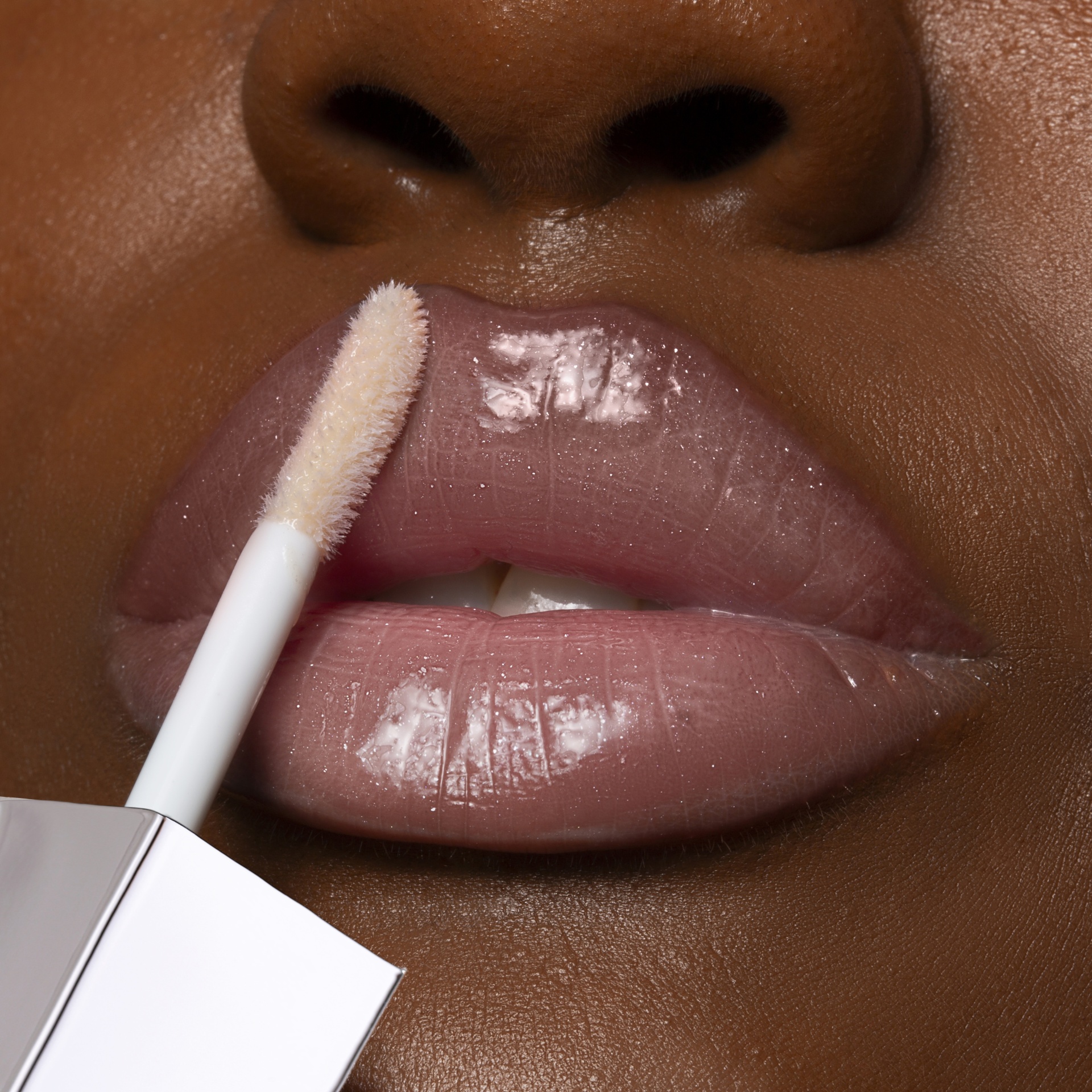Gloss Lara Beauty Aplicador branco a aplicar gloss labial translúcido em lábios castanhos.