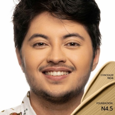 Homem sorrindo segurando amostras de base e corretor de tons bege