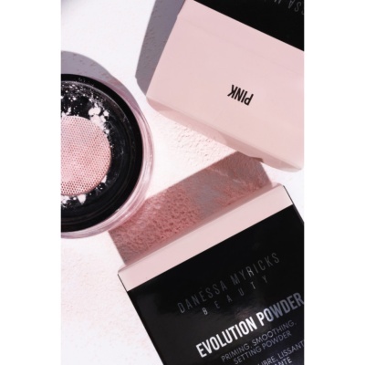 Pó solto translúcido Danessa Myricks Beauty Evolution Powder com embalagem preta e rosa sobre superfície clara