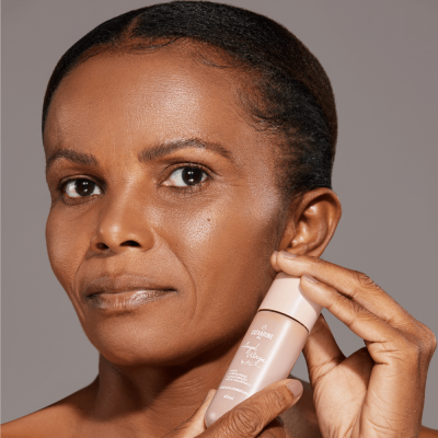 Mulher segurando recipiente de produto cosmético rosa claro com texto branco