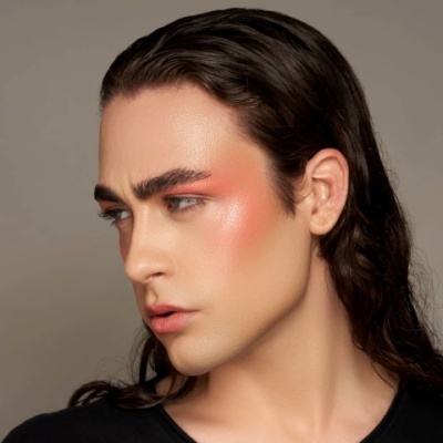 Rosto com maquilhagem em tons de coral e rosa, cabelo castanho comprido e roupa preta