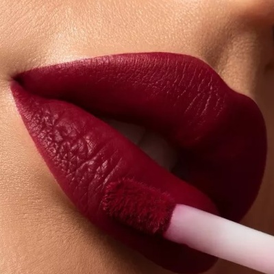 Lábios a receber aplicação de batom líquido bordô com aplicador de esponja