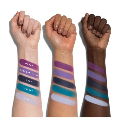 Três braços com diferentes tons de pele e amostras coloridas de maquiagem em faixas horizontais com texto