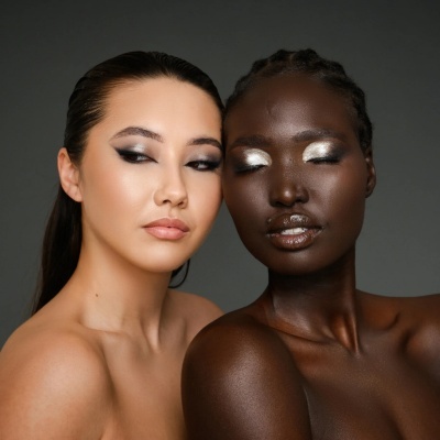 Duas mulheres com maquilhagem distinta e fundo cinzento.