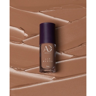 Frasco de lip blush AG Beauty cor bege castanho sobre textura cremosa