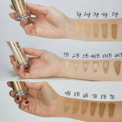 Braços com diferentes tons de base líquida aplicados e frascos do produto