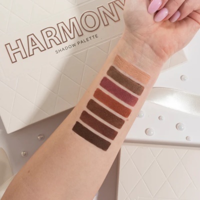 Paleta de sombras 'HARMONY SHADOW PALETTE' com sete tons terra aplicados no braço em cima da embalagem.