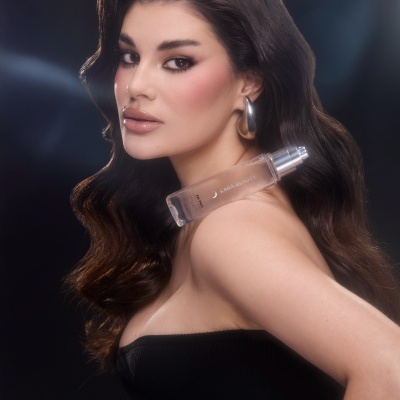 Frasco de perfume transparente com texto LARA BEAUTY junto ao ombro de mulher com cabelo castanho escuro e vestido preto