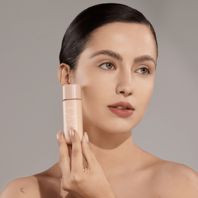 Mulher segurando frasco de creme facial bege claro com tampa rosada perto do rosto