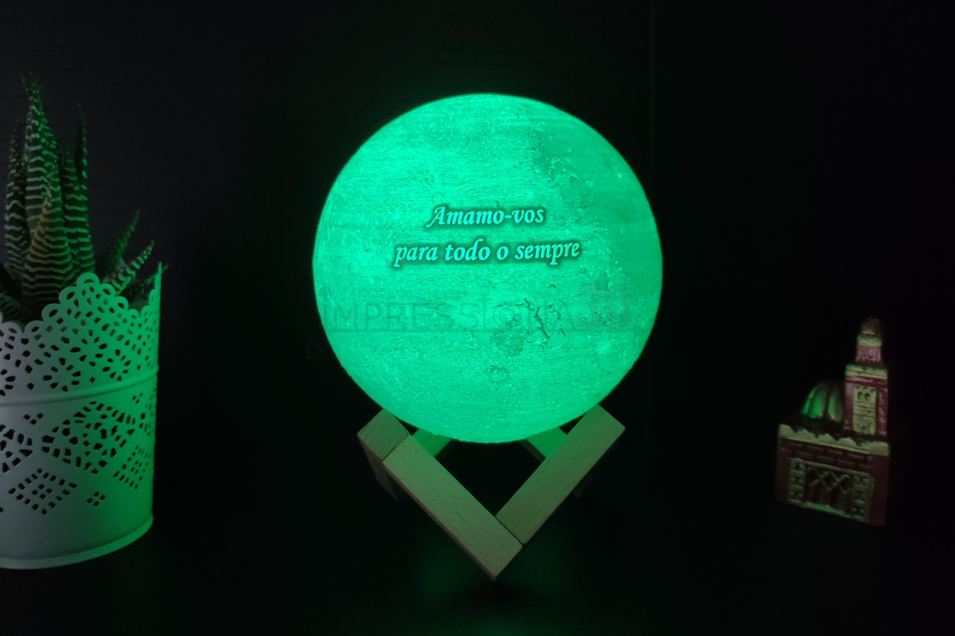 Globo iluminado verde com texto e base de madeira entre objetos decorativos