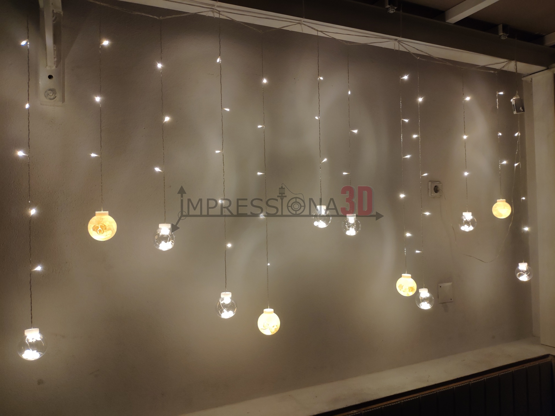 Lâmpadas penduradas com bolas brancas e formas transparentes acesas contra parede cinza claro