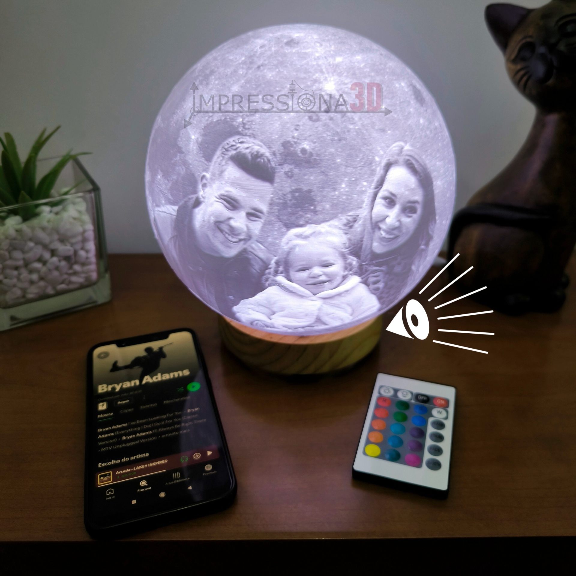Globo lunar iluminado com foto personalizada, base de madeira, comando remoto e smartphone numa mesa