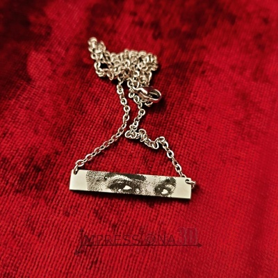 Colar prateado com pendente retangular estampado com olhos, sobre fundo vermelho