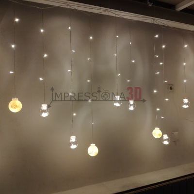 Lâmpadas penduradas com bolas brancas e formas transparentes acesas contra parede cinza claro