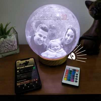 Globo lunar iluminado com foto personalizada, base de madeira, comando remoto e smartphone numa mesa