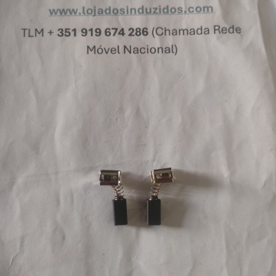 Duas escovas de carvão com molas e terminais metálicos sobre papel com texto impresso.