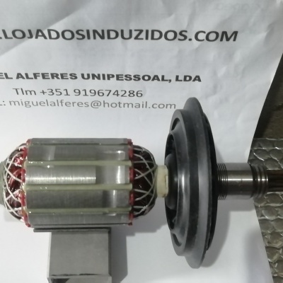 Peça metálica cilíndrica com enrolamentos vermelhos e cobre sobre superfície metálica texturada.