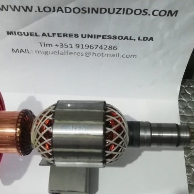 Peça mecânica cilíndrica com cobre, metal e plástico vermelho sobre fundo texturizado prateado, papel com texto impresso ao fundo