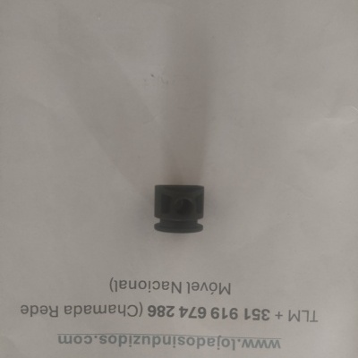 Peça mecânica preta cilíndrica sobre papel branco com texto impresso.