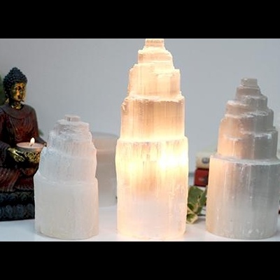 Três velas de selenite translúcidas e uma estátua de Buda com vela acesa em fundo branco