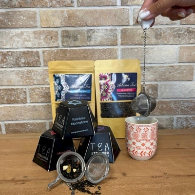 Pacotes de chá dourados, caixas pretas de infusores, infusores metálicos e copo cerâmico decorado