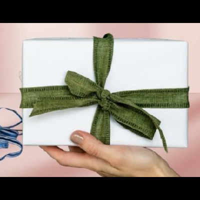 Caixa branca com fita verde em laço segurada por uma mão, com fita azul solta ao lado