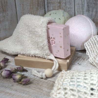 Conjunto de produtos de higiene pessoal com sabão rosa, esferas efervescentes, saco de tecido e flores secas.