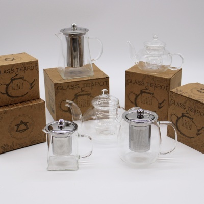 Vários bules de vidro com infusores metálicos e caixas de papel kraft rotuladas