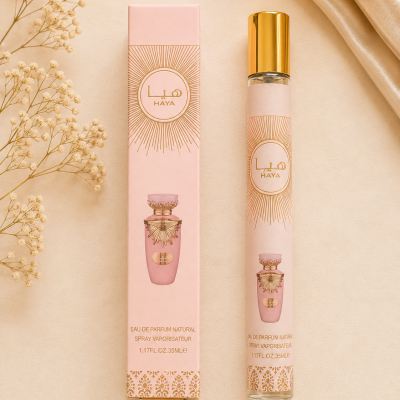 Frasco e caixa de perfume HAYA em rosa e dourado sobre superfície bege com flores e tecido acetinado