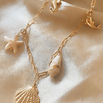 Colar dourado com pendentes marinhos sobre tecido acetinado
