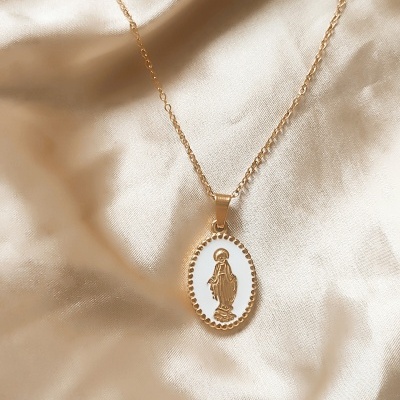 Colar dourado com pendente oval e figura religiosa, sobre tecido acetinado dourado