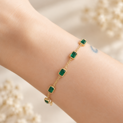 Pulseira dourada com pedras verdes quadradas no pulso