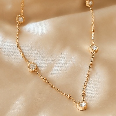 Colar fino dourado com pedras transparentes em tecido de cetim bege