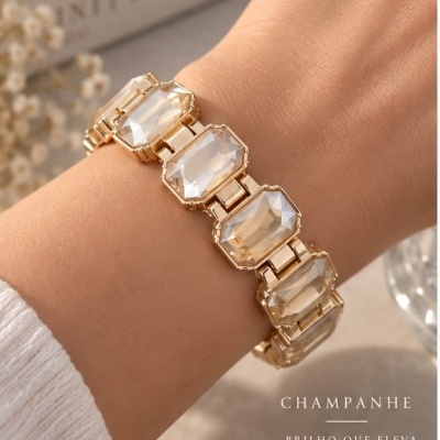 Pulseira dourada com pedras transparentes grandes retangulares num pulso